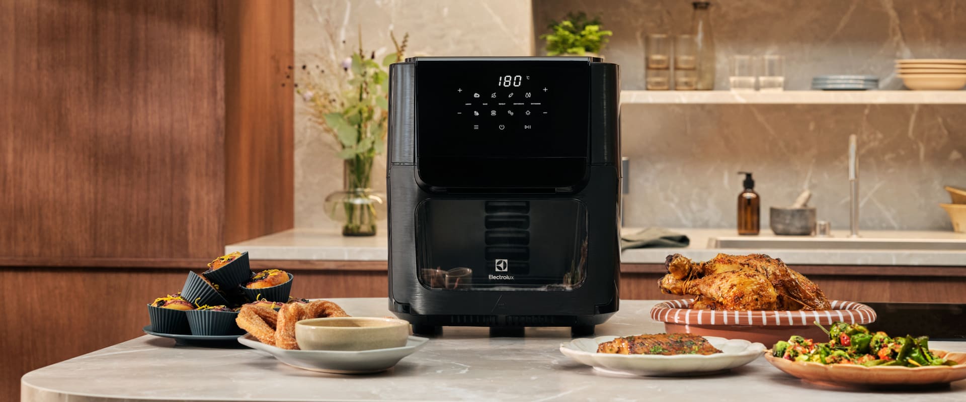 Zdjęcie air fryera Electrolux na kuchennym blacie obok pysznie wyglądających potraw